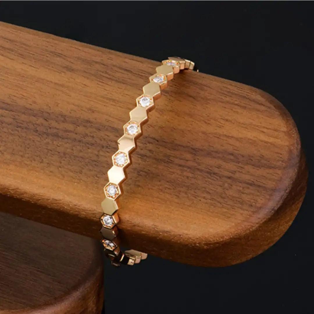 Mozi Beehive Moissanite Bangle draped over a wooden surface, showcasing its hexagonal gold design with moissanite stones