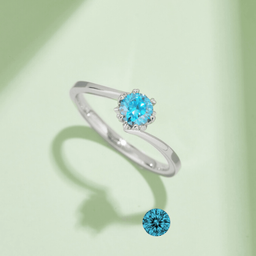 Close-up of the Blue Flower Moissanite Ring showcasing its brilliant round blue Moissanite set in a floral design on a light green background.