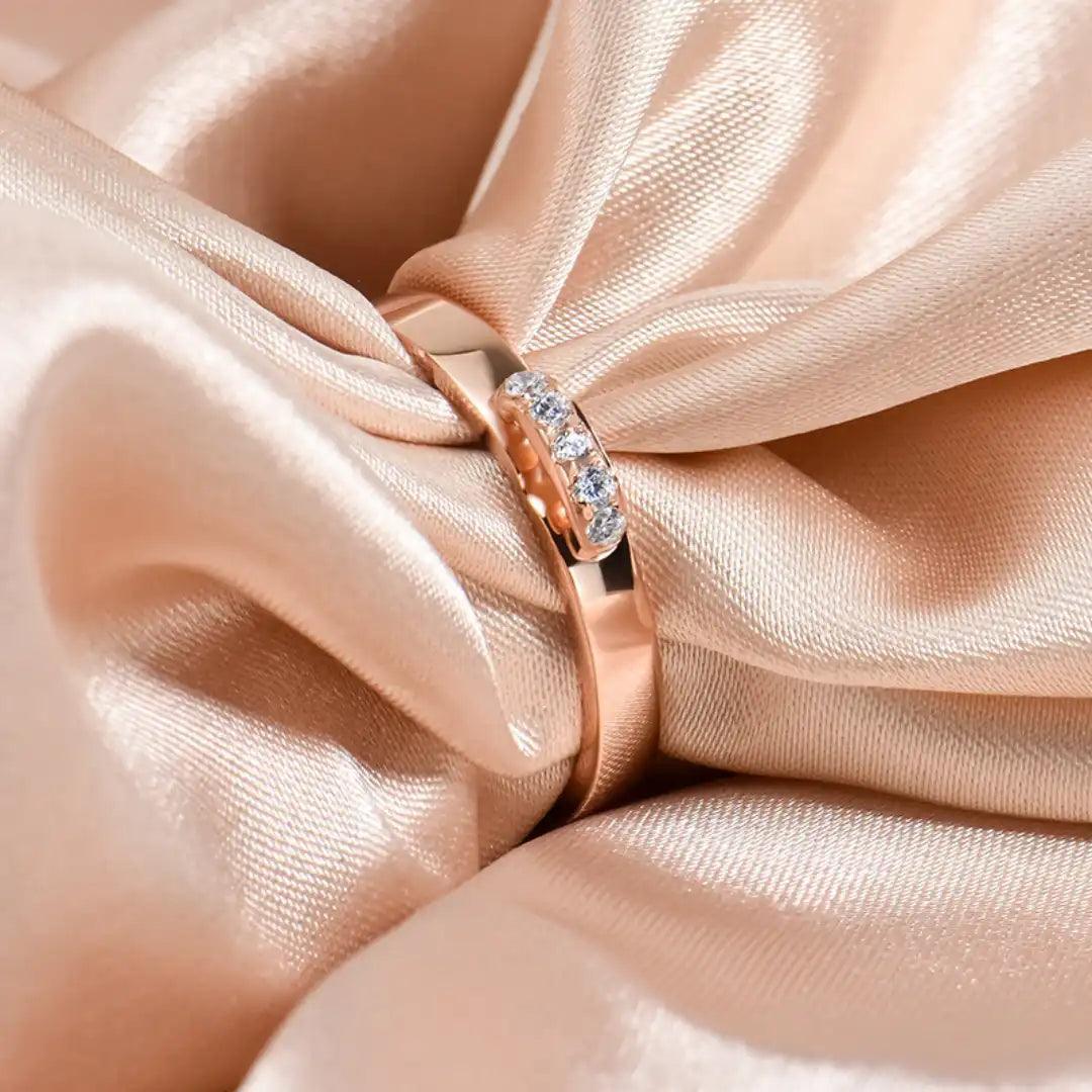 Rose gold ring with moissanite stones displayed elegantly on a soft, peach-colored satin fabric.