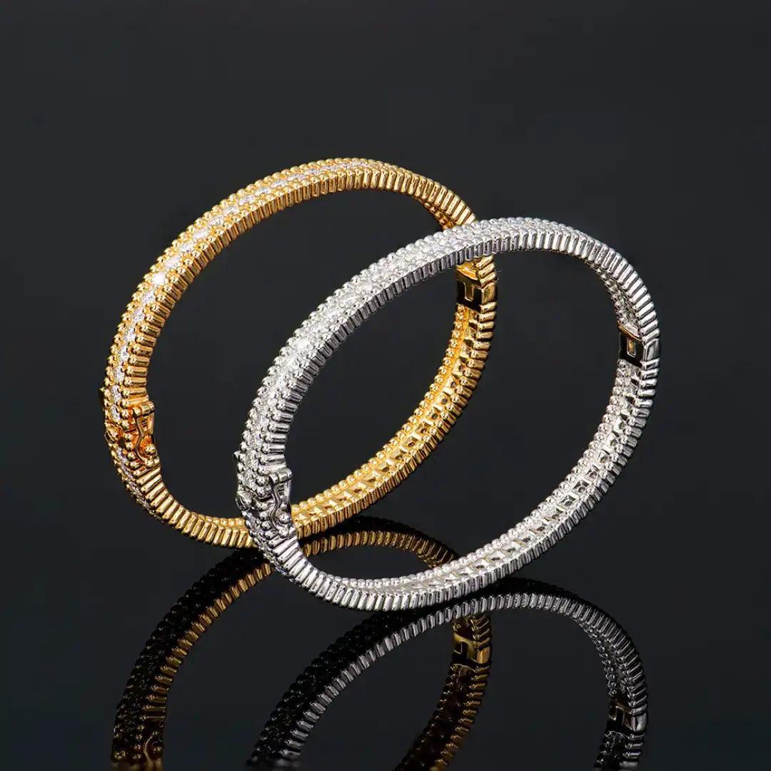 A pair of Mozi Celestial Moissanite Bangles in gold and silver displayed on a black reflective surface, showcasing the detailed craftsmanship and sparkling moissanite stones.