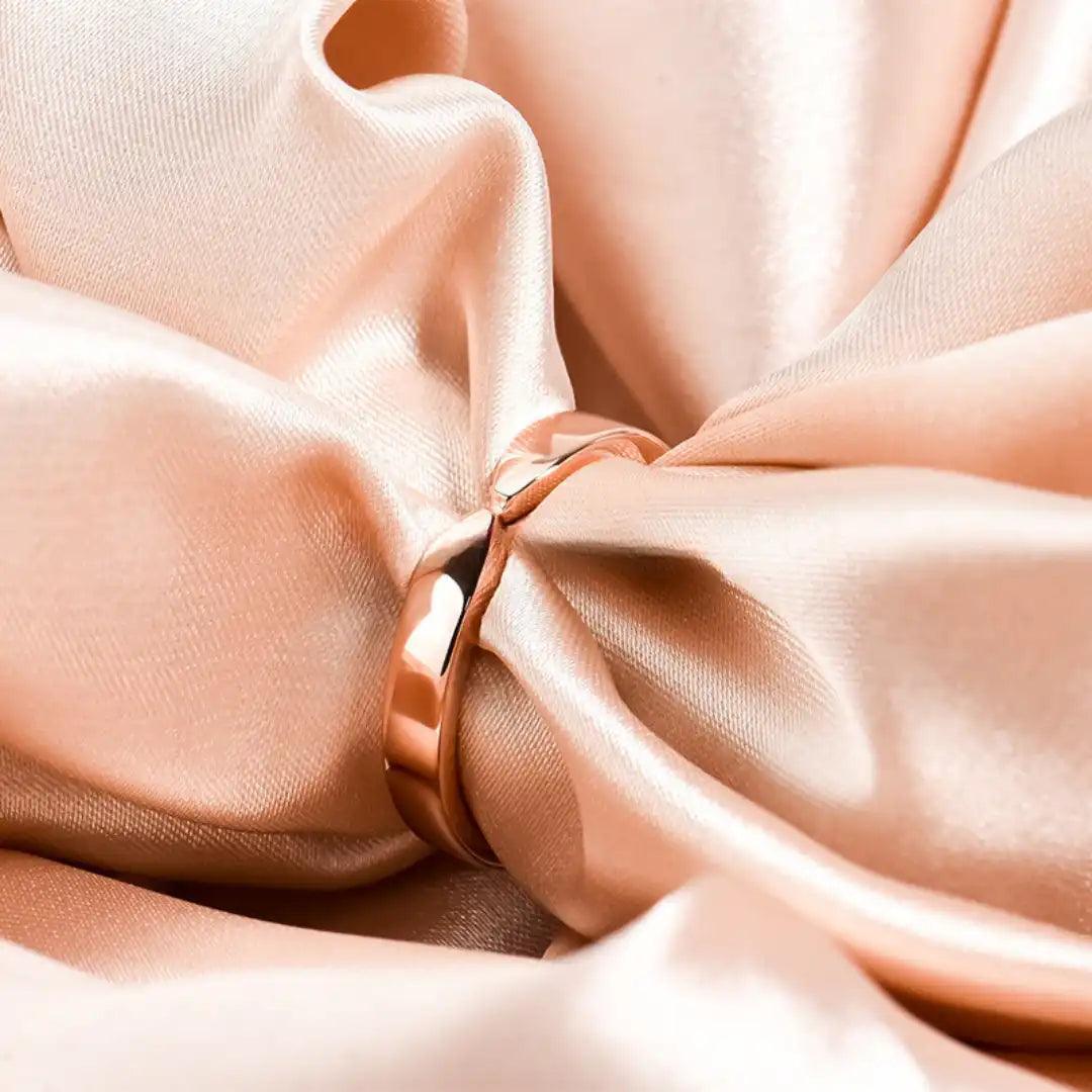 Rose gold twist ring placed on a soft, peach-colored fabric, highlighting its smooth and reflective surface.