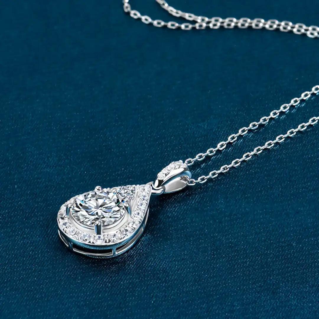 Teardrop Moissanite Necklace laid flat on a teal background, emphasizing the pendant's luxurious design and sparkling moissanite stone.