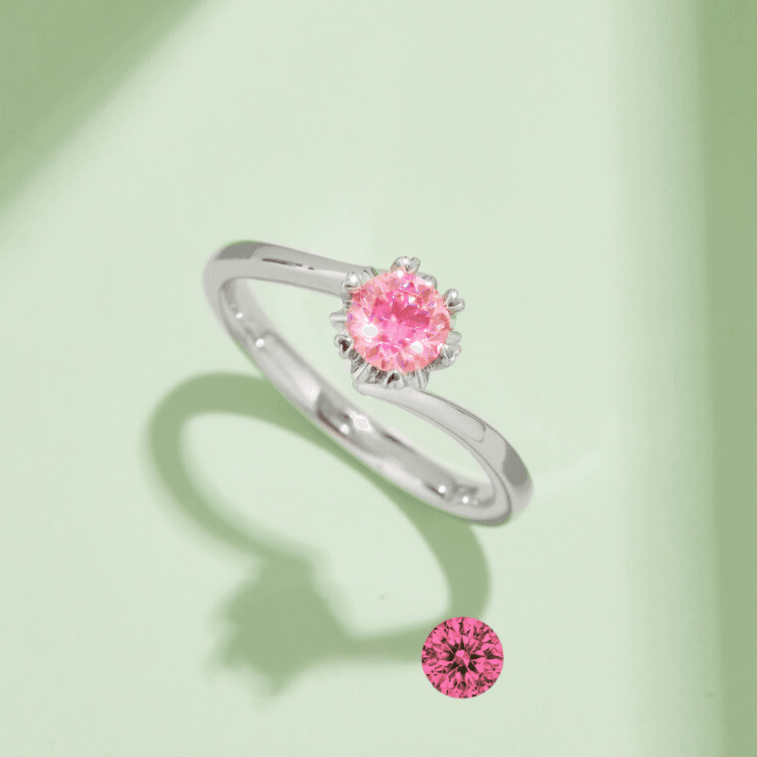 Close-up of the Pink Flower Moissanite Ring from the Flower Collection showcasing its brilliant round pink Moissanite set in a floral design on a light green background.