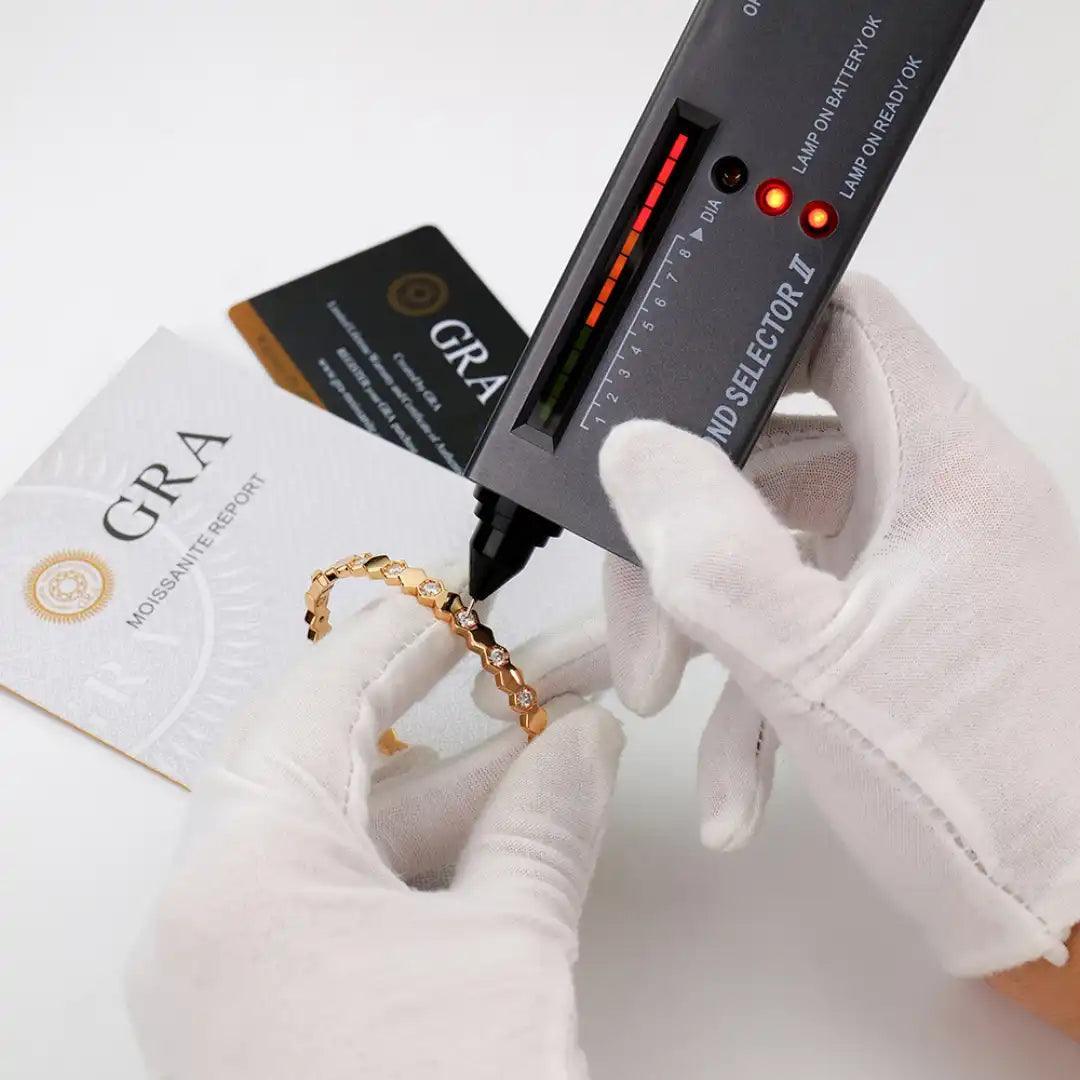 Mozi Beehive Moissanite Bangle being tested with a diamond selector tool by gloved hands, with a GRA moissanite report in the background