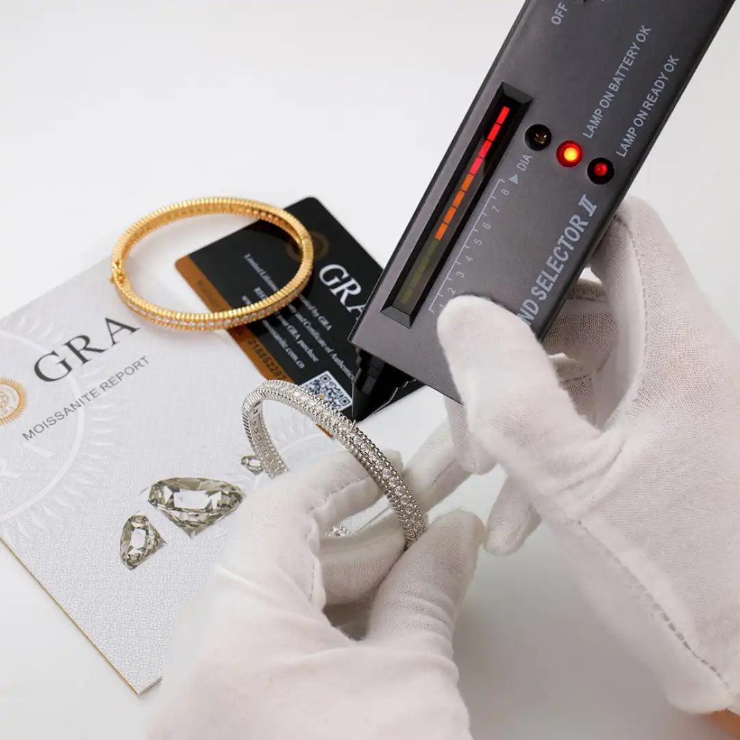 Mozi Celestial Moissanite Bangles being tested for authenticity with a diamond tester, accompanied by a GRA certificate and card, showcasing the quality and craftsmanship of the gold and silver bangles